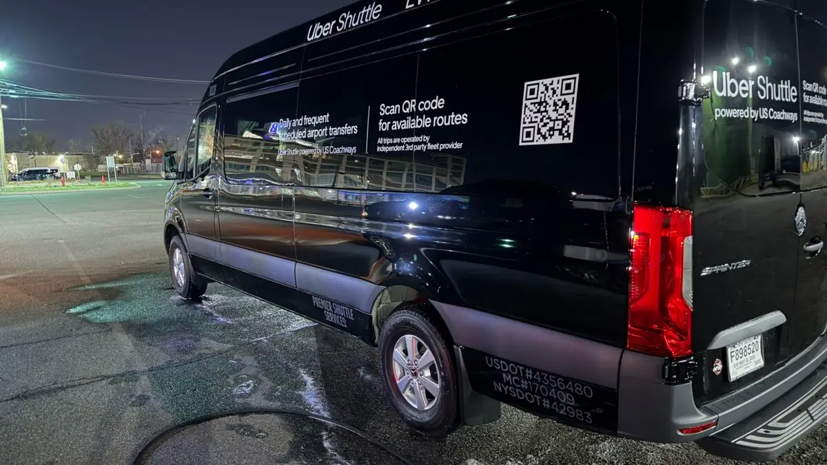 A freshly washed black Mercedes-Benz Sprinter with Uber Shuttle branding, parked at night.